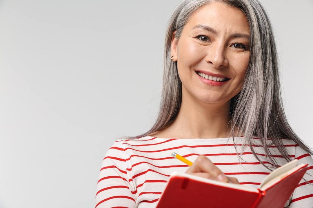 lady with dental implants smiling while writing on her red booklet