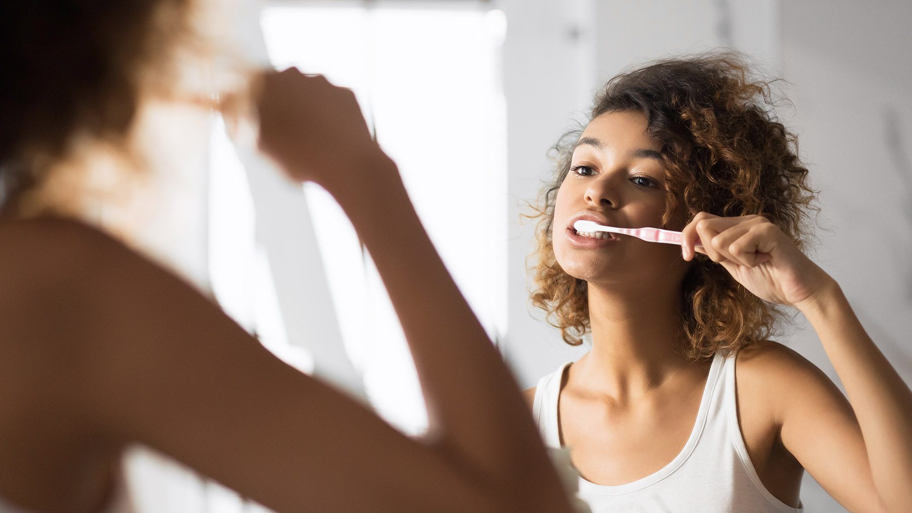 woman brushing her teeth infront of mirror